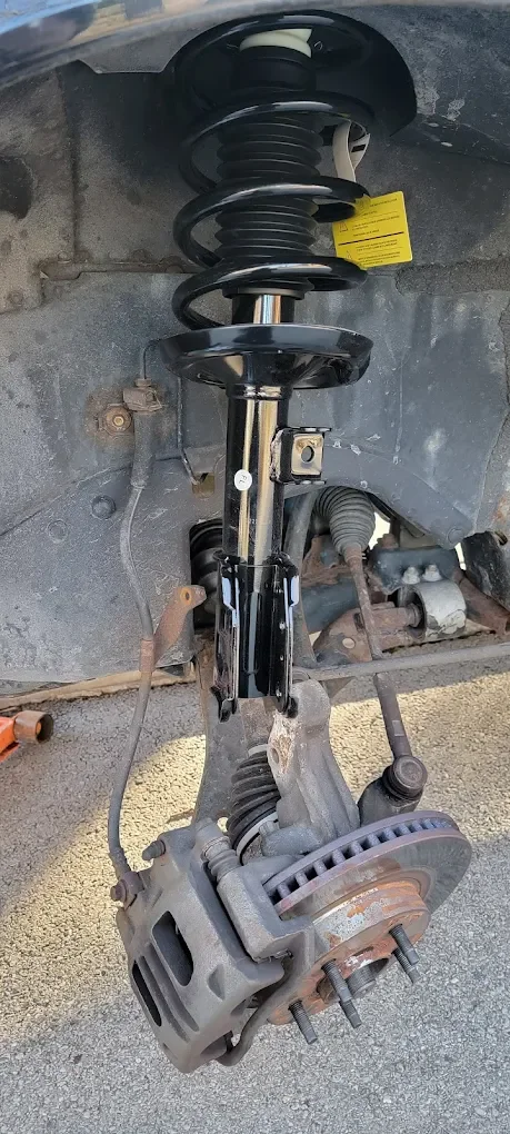 A car's front suspension system with brake caliper, rotor, coil spring, shock absorber, and control arms.