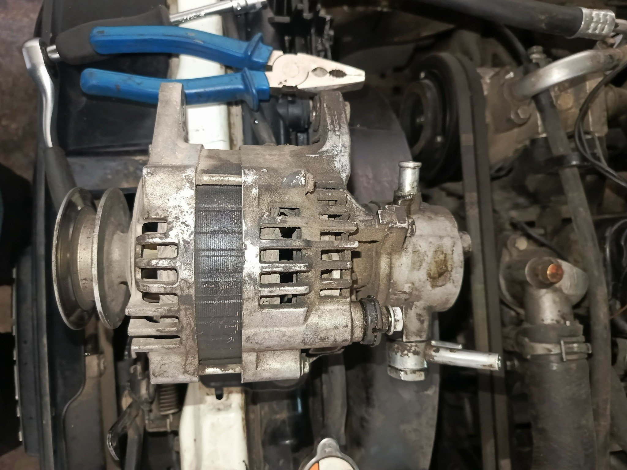 A car alternator on a workbench with pliers and other tools nearby.