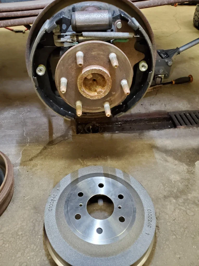 A disc brake rotor removed from a vehicle, with the backer plate and brake caliper assembly above it, on a concrete floor.
