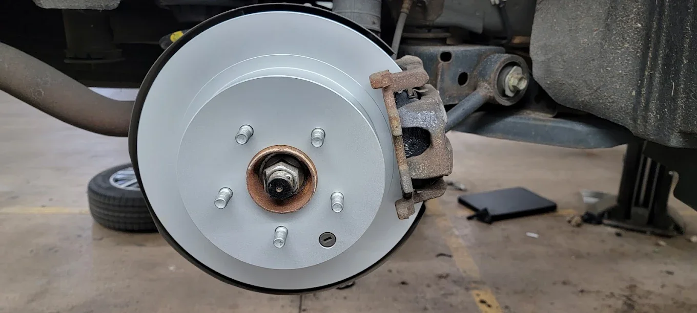 A car's brake disc and caliper assembly with the wheel removed, showing the brake rotor and mounting hub.