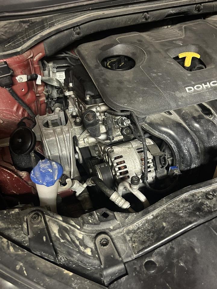 View of a car engine with a black plastic cover labeled 'DOHC', part of the engine block, hoses, and a yellow oil filler cap showing.