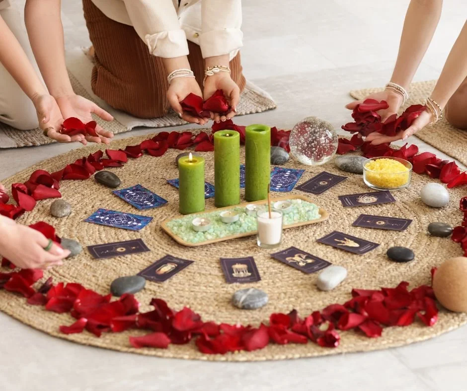 People conducting a spiritual or tarot reading on a circular rug with candles, stones, cards, and rose petals.