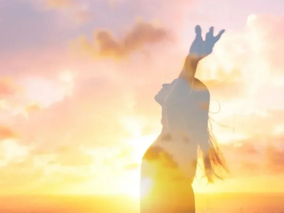 Silhouette of a woman with long hair raising her hand against a sunset sky with clouds