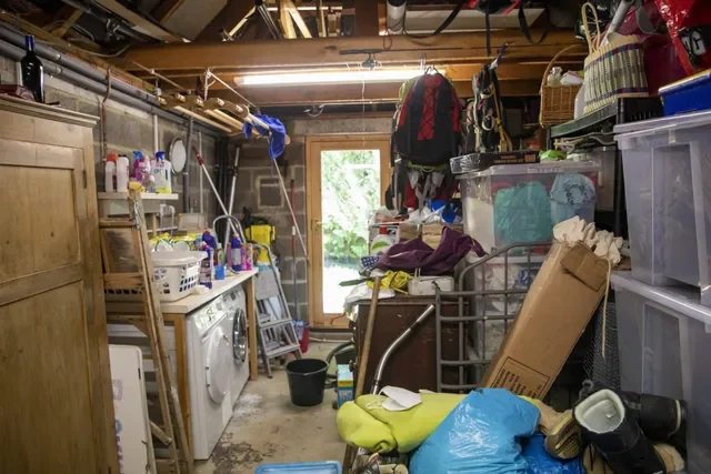 Cluttered laundry room with washer and dryer, storage bins, cleaning supplies, and miscellaneous household items.