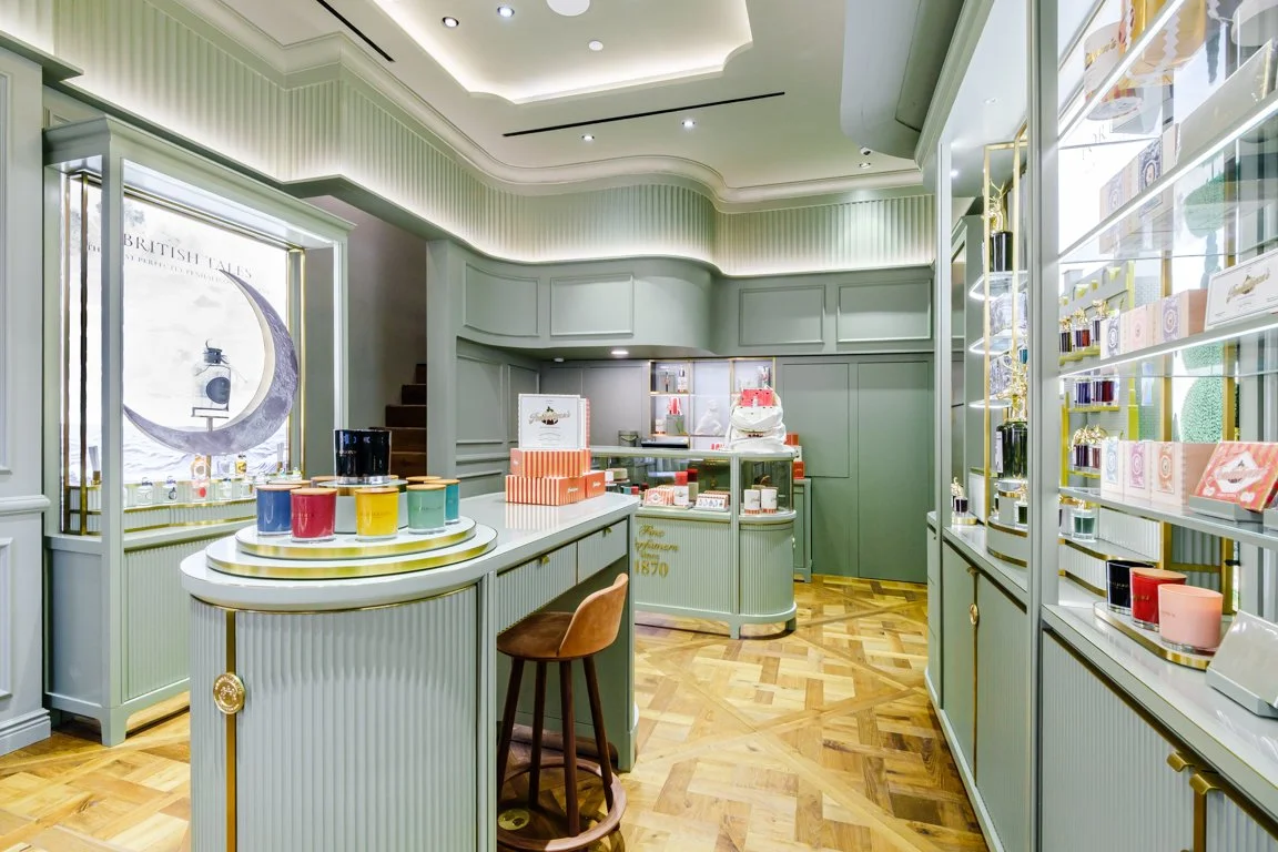 Interior of a boutique store with mint green cabinetry, wooden flooring, and soft lighting. Shelves and display cases showcase various colorful products and packaging.