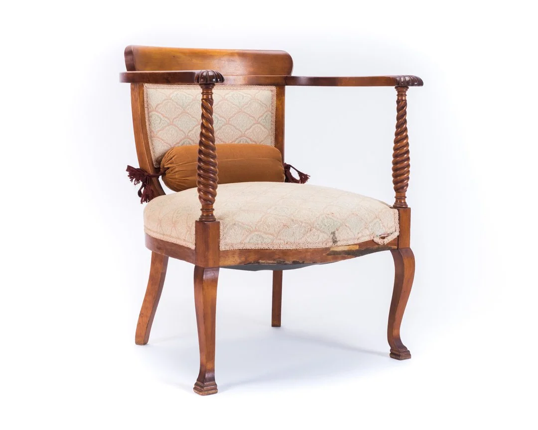 Vintage wooden armchair with upholstered seat and back, decorative twisted armrest supports, and a small brown cushion.