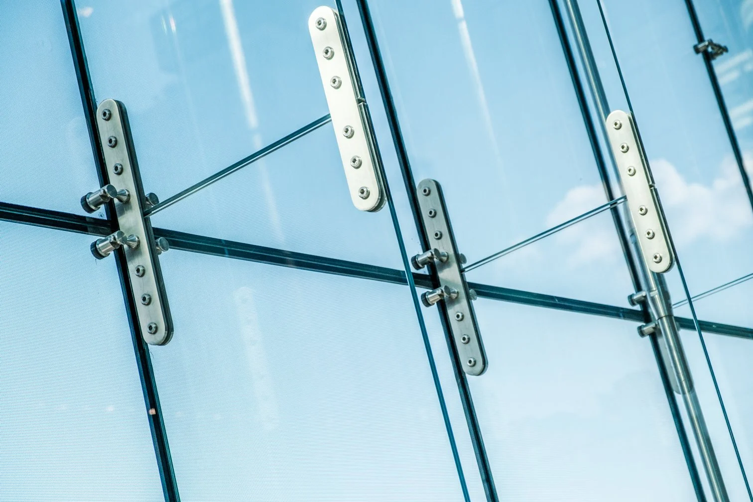 Close-up view of modern glass building exterior with metal fixtures and visible reflection of sky and clouds.