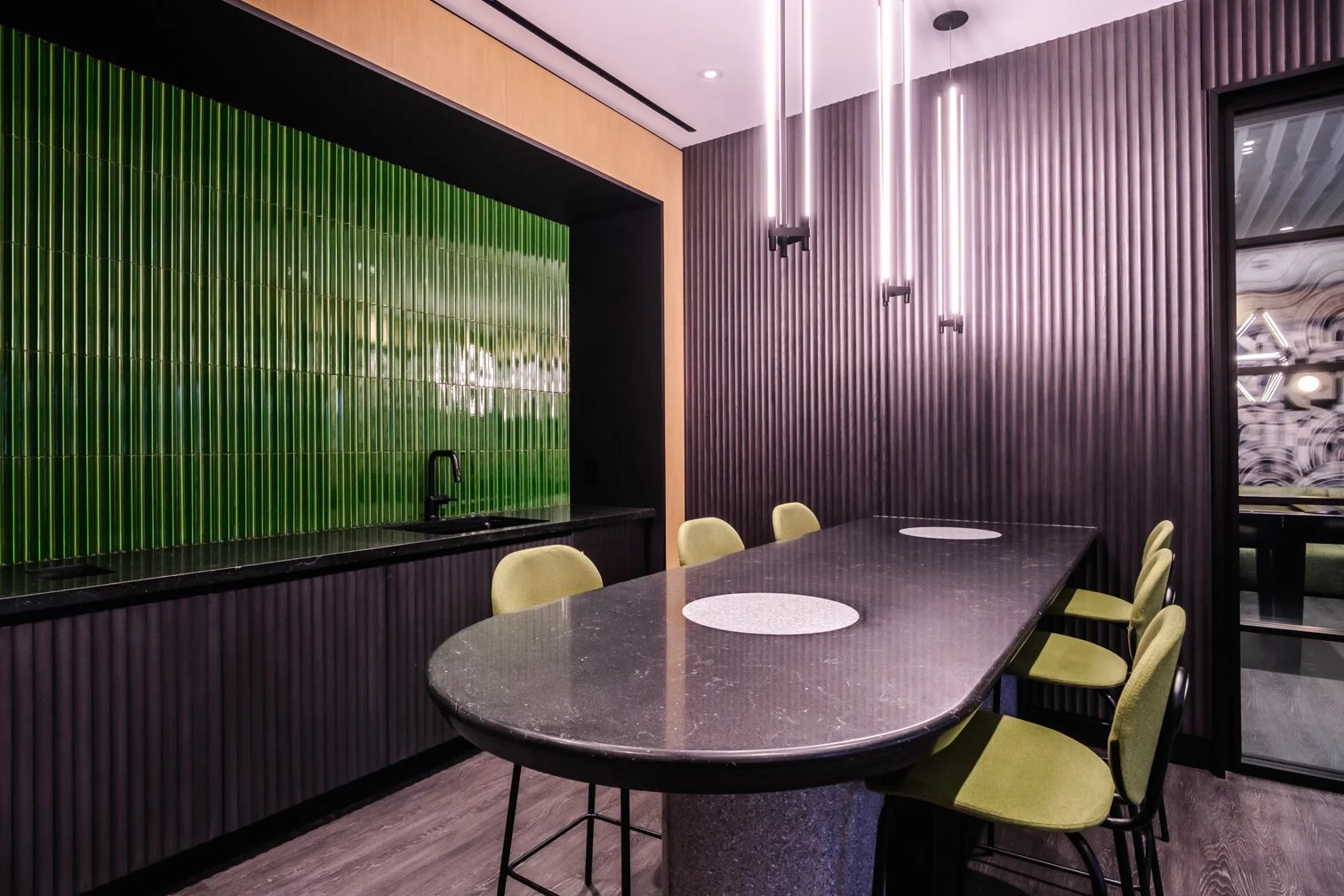 Modern dining room with a long black marble table, green and purple textured wall panels, hanging vertical light fixtures, and yellow chairs.