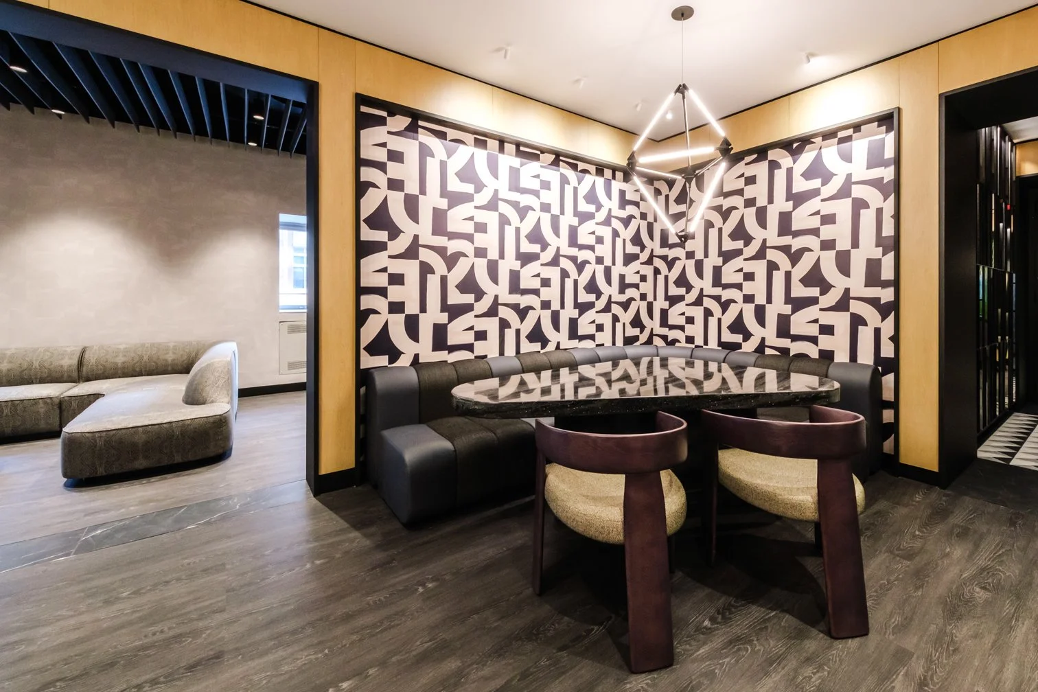Modern lounge with a patterned accent wall, a round table surrounded by chairs, and a seating area with an L-shaped sofa, in a stylish interior design.