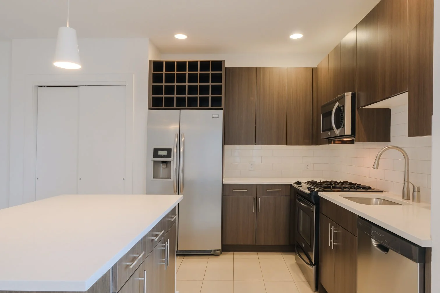 Modern kitchen with wooden cabinets, stainless steel appliances, a white countertop, and a tiled backsplash.