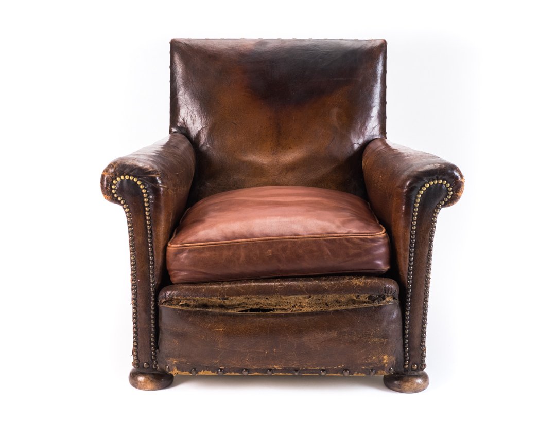Old brown leather armchair with worn armrests and a cushion, isolated on a white background.