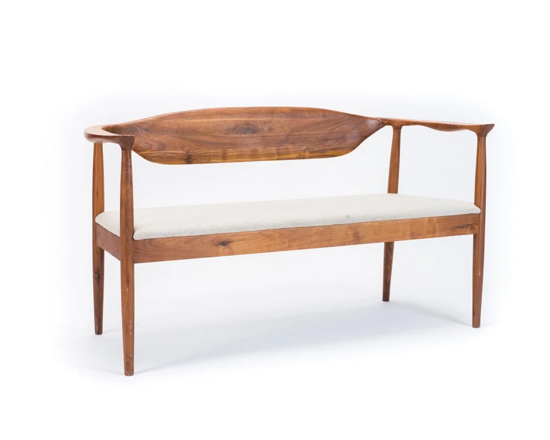 A mid-century modern wooden bench with a cushioned seat and a curved backrest against a white background.