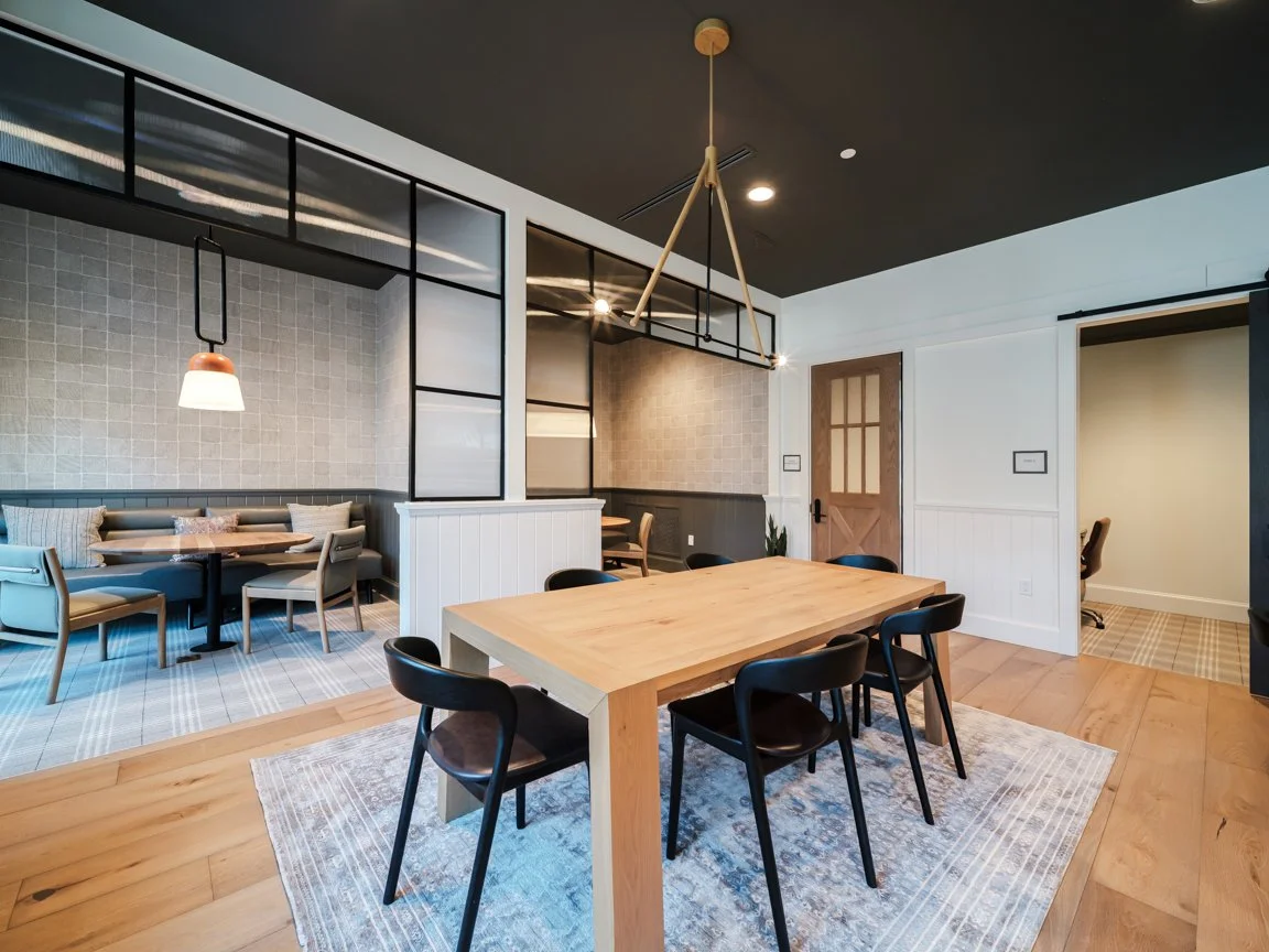Modern dining room with wooden table and black chairs, with a sitting nook in the background and decorative lighting fixtures, in a contemporary style.