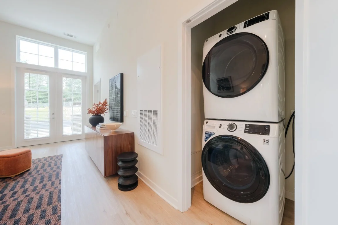 Stacked front-loading washer and dryer in a small laundry nook inside a modern home.