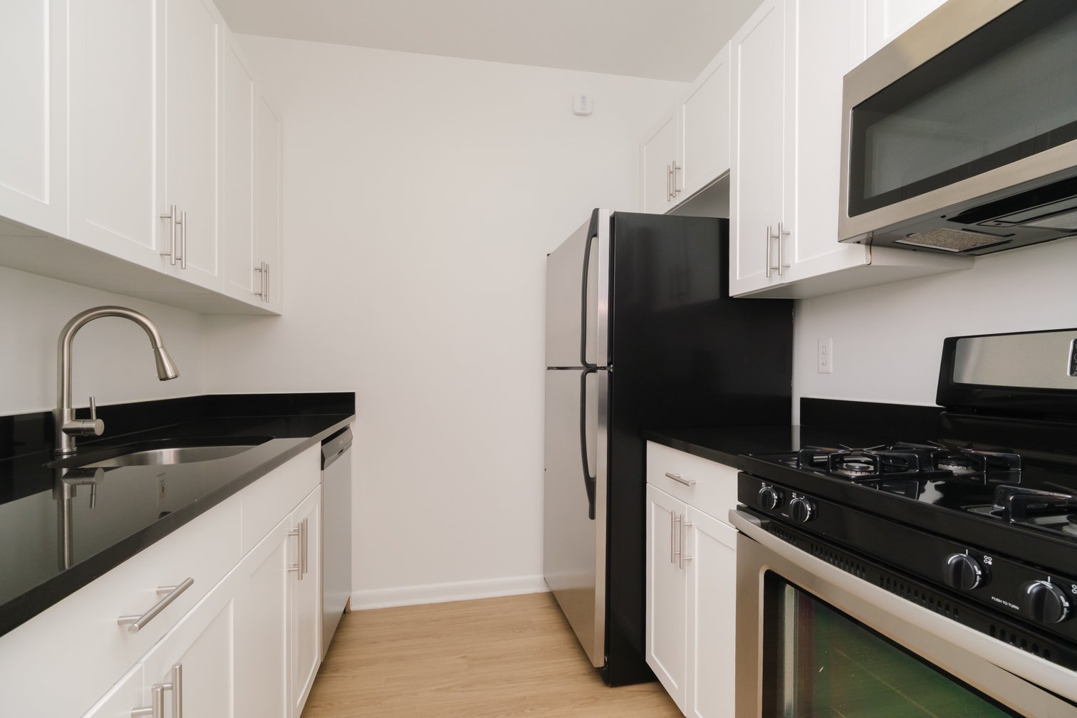 Modern kitchen with white cabinets, black countertops, stainless steel refrigerator, microwave, oven, and a black sink.