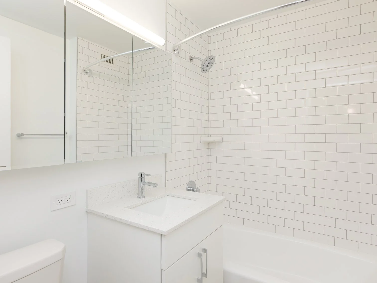 Modern bathroom with white subway tiles, a showerhead, a mirror, a white vanity with a sink, and a white toilet.