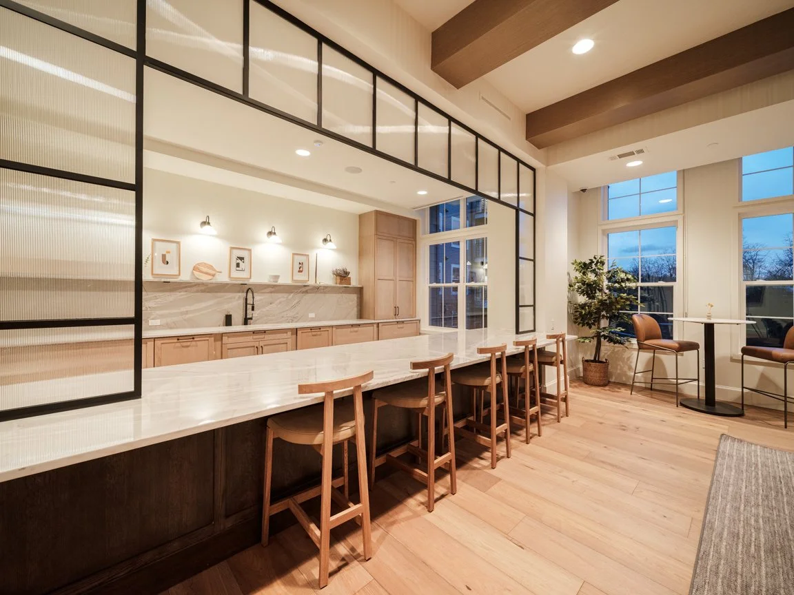Modern kitchen and dining area with high countertop, bar stools, large windows, and a potted plant.