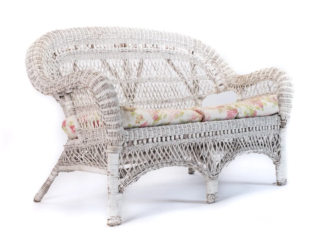 White wicker loveseat with floral cushion on a white background.