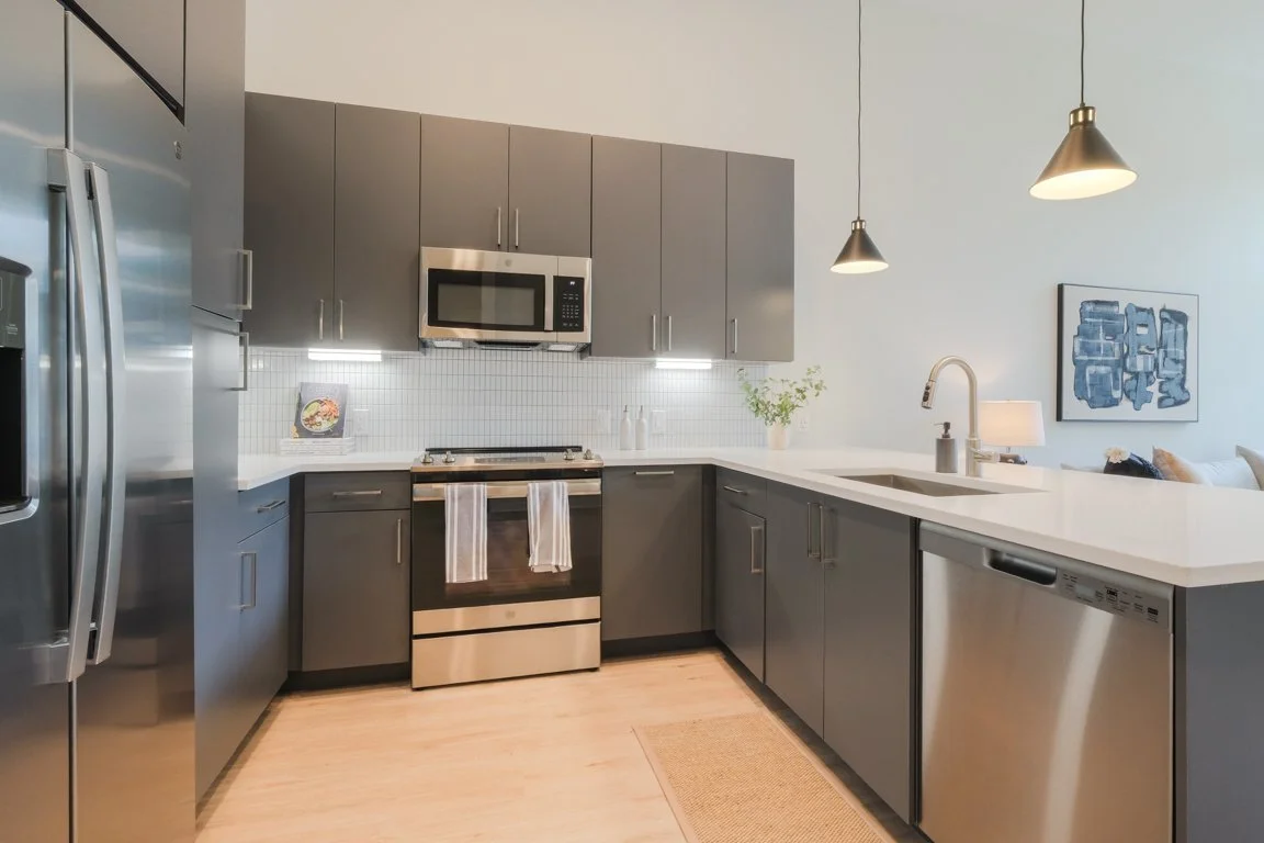 Modern kitchen with gray cabinets, stainless steel appliances, white countertops, pendant lights, a sink with a faucet, and wall art.