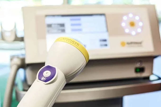 Medical device in a hospital setting, with a screen displaying information and a white and yellow handheld instrument labeled 'non-focused' in the foreground.