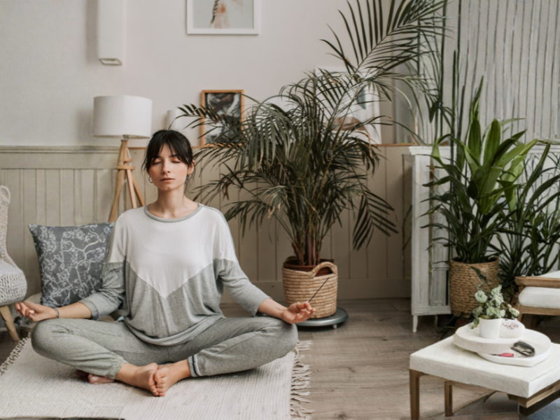 Eine Frau sitzt auf ihrer Yoga Matte und führt Pranayama/Breathwork aus