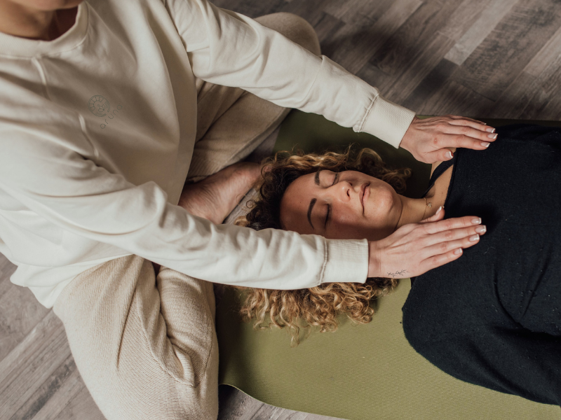Eine Frau liegt auf einer Yoga Matte und bekommt eine Reiki Anwendung
