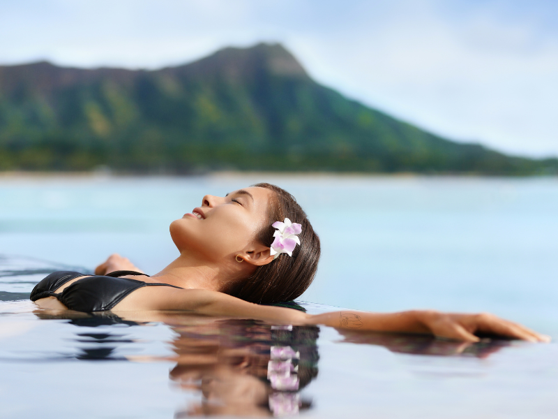 Eine Frau schwebt im Meer vor Hawaii, im Hintergrund ein begrünter Berg