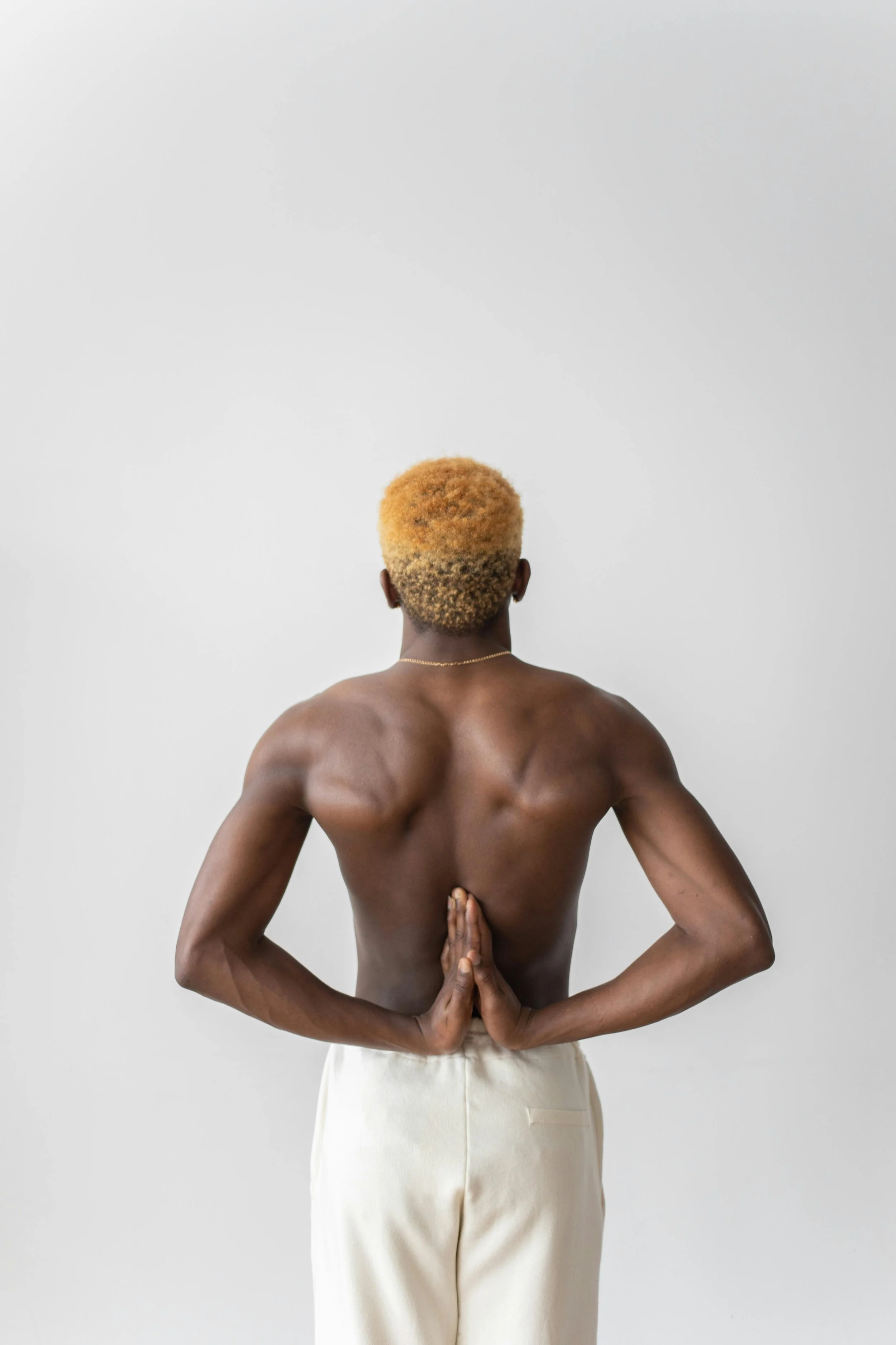 Ein Mann steht in einer Yoga Pose mit auf dem Rücken gefalteten Händen