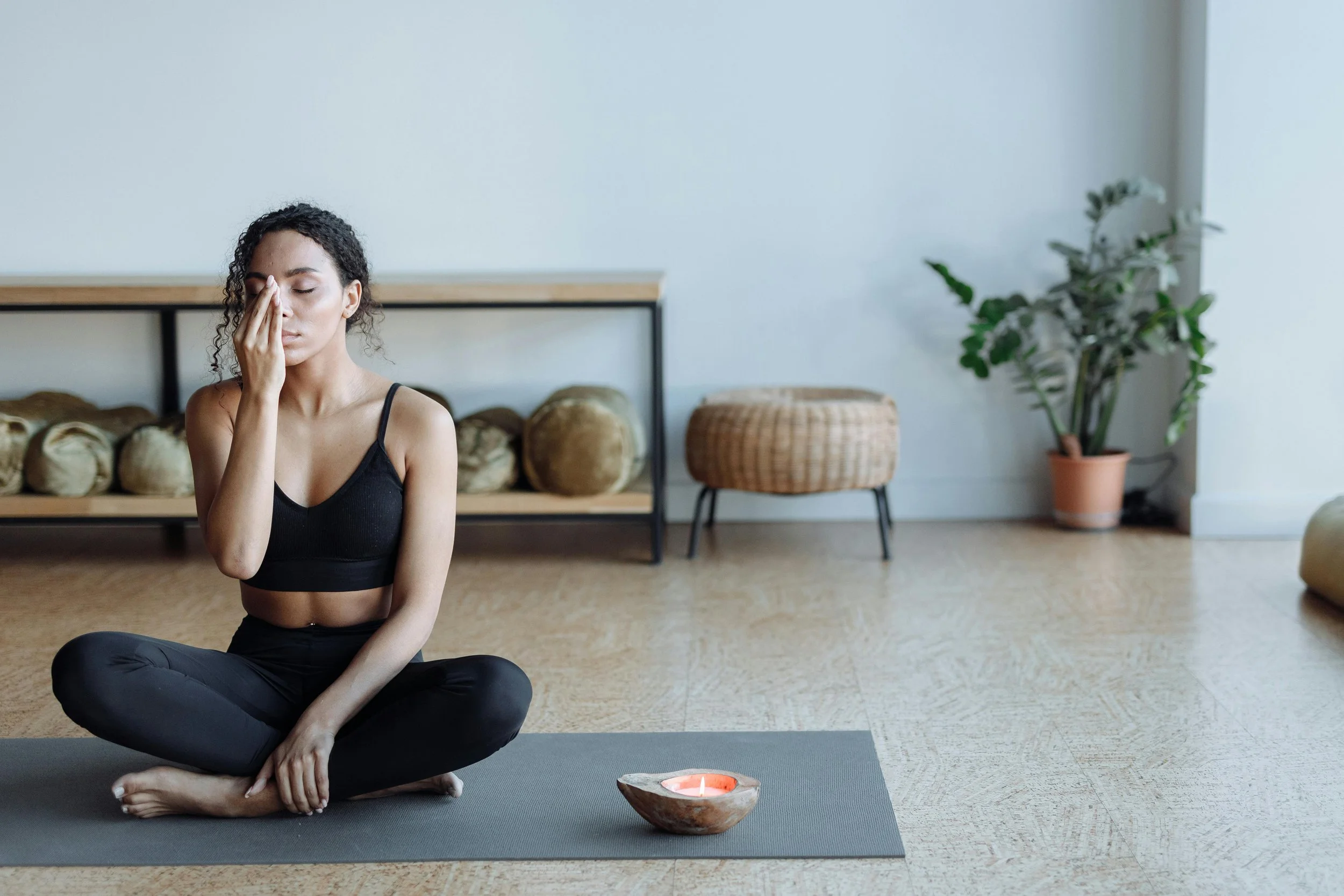 Frau sitzt neben einer Kerze auf Yoga Matte und führt Pranayama/Breathwork aus