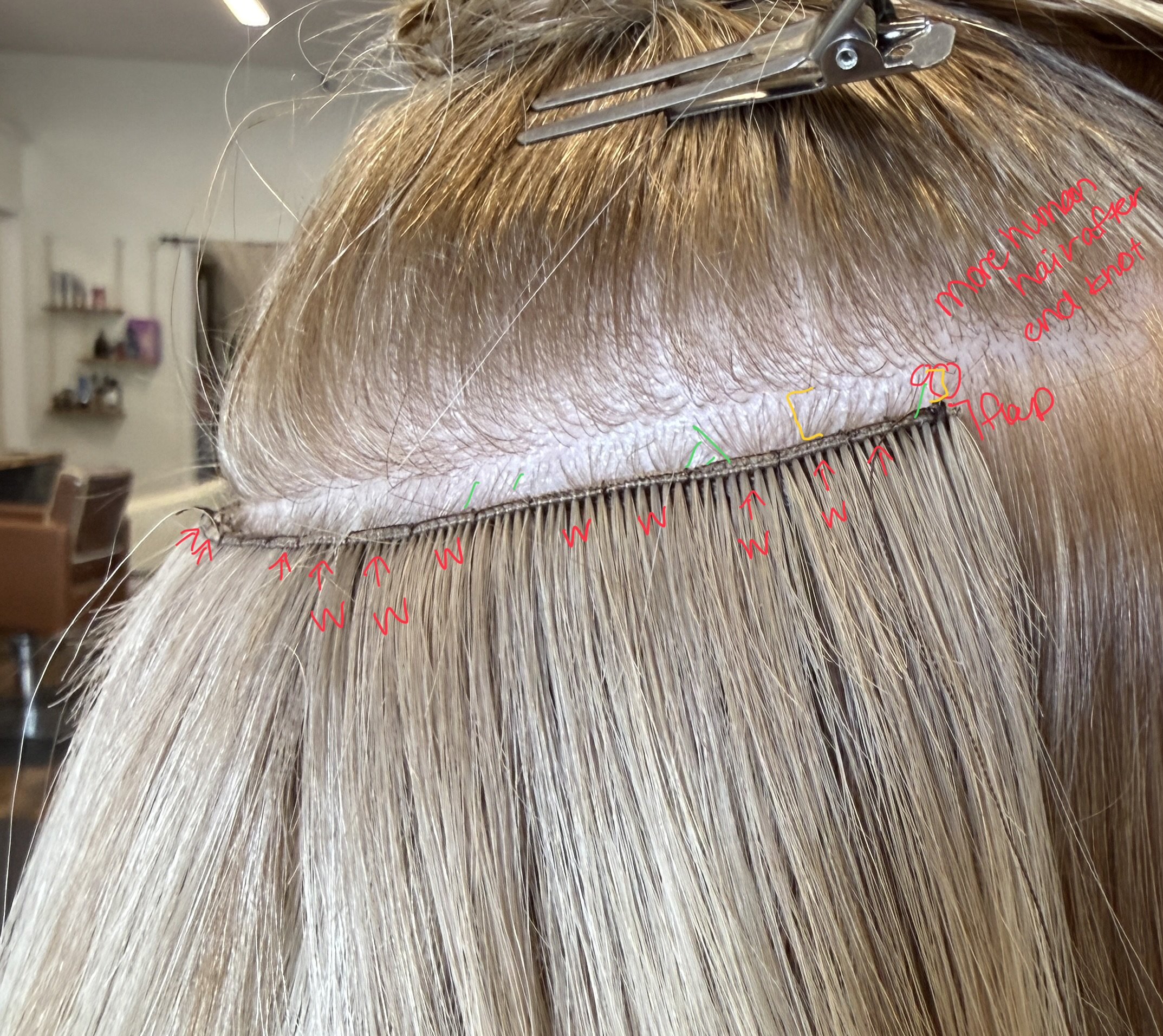 Close-up of hair with a hairbrush, strip of hair extensions, and annotations in red, green, and yellow writing, possibly for hair styling or extension application.