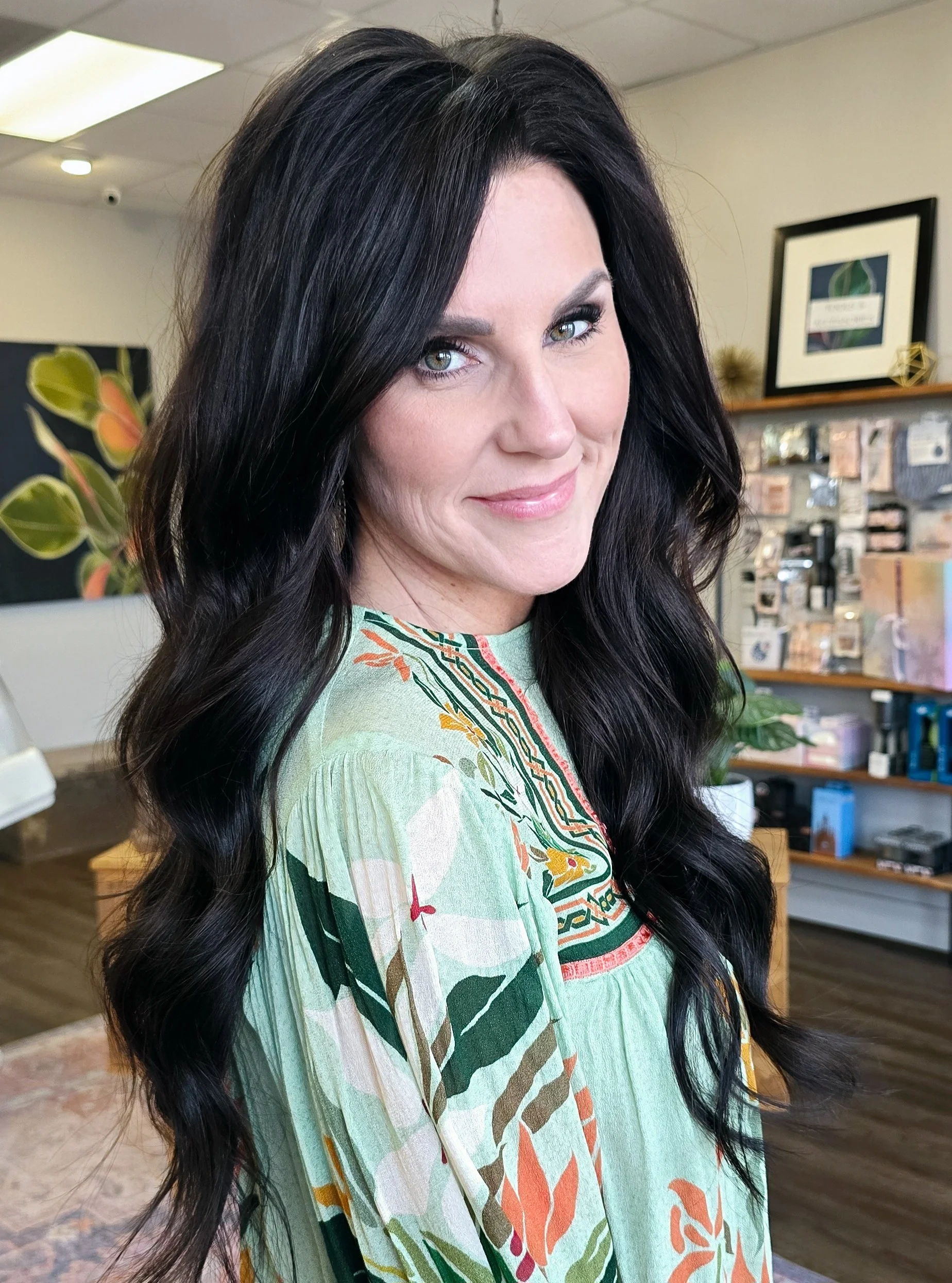 A Luna Method client with long, wavy dark hair smiling while looking at the camera in a luxury salon with art and decor in the background.