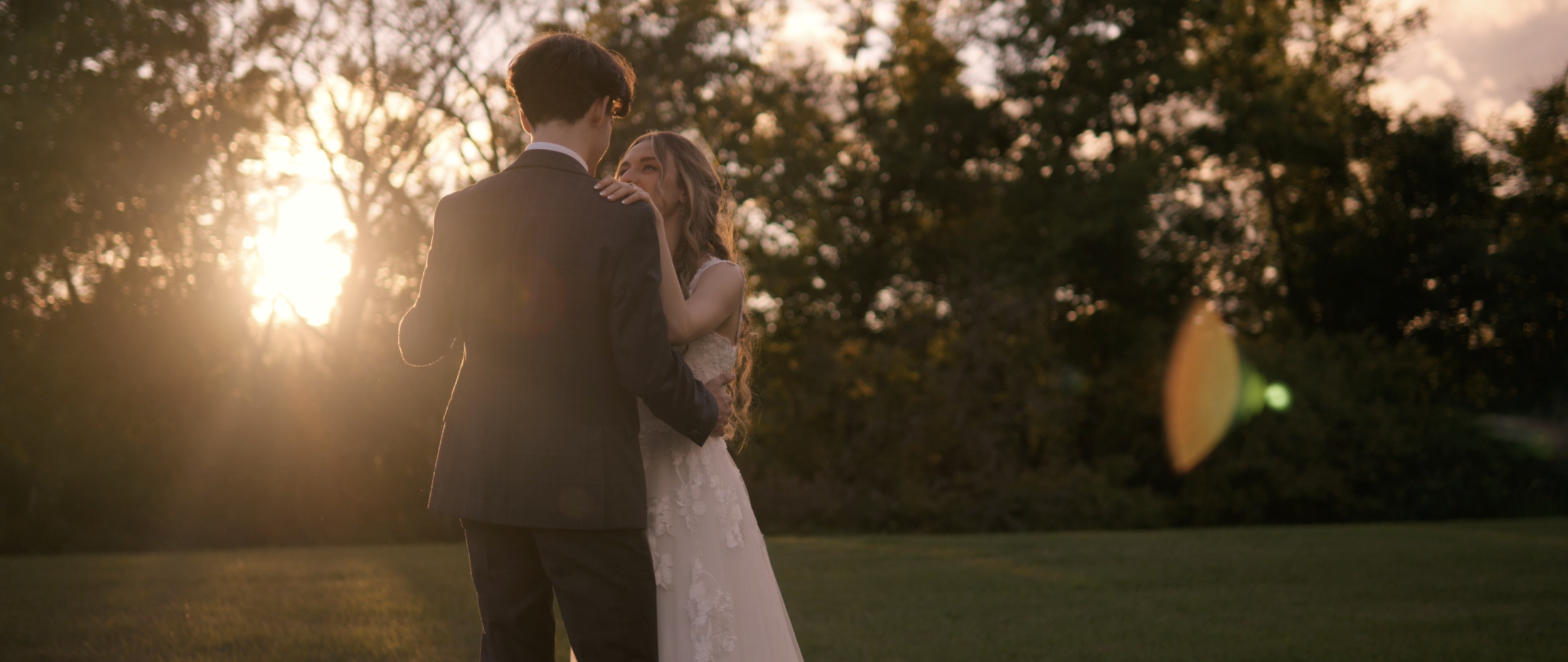 A bride and groom sharing a dance outdoors during sunset, surrounded by trees.