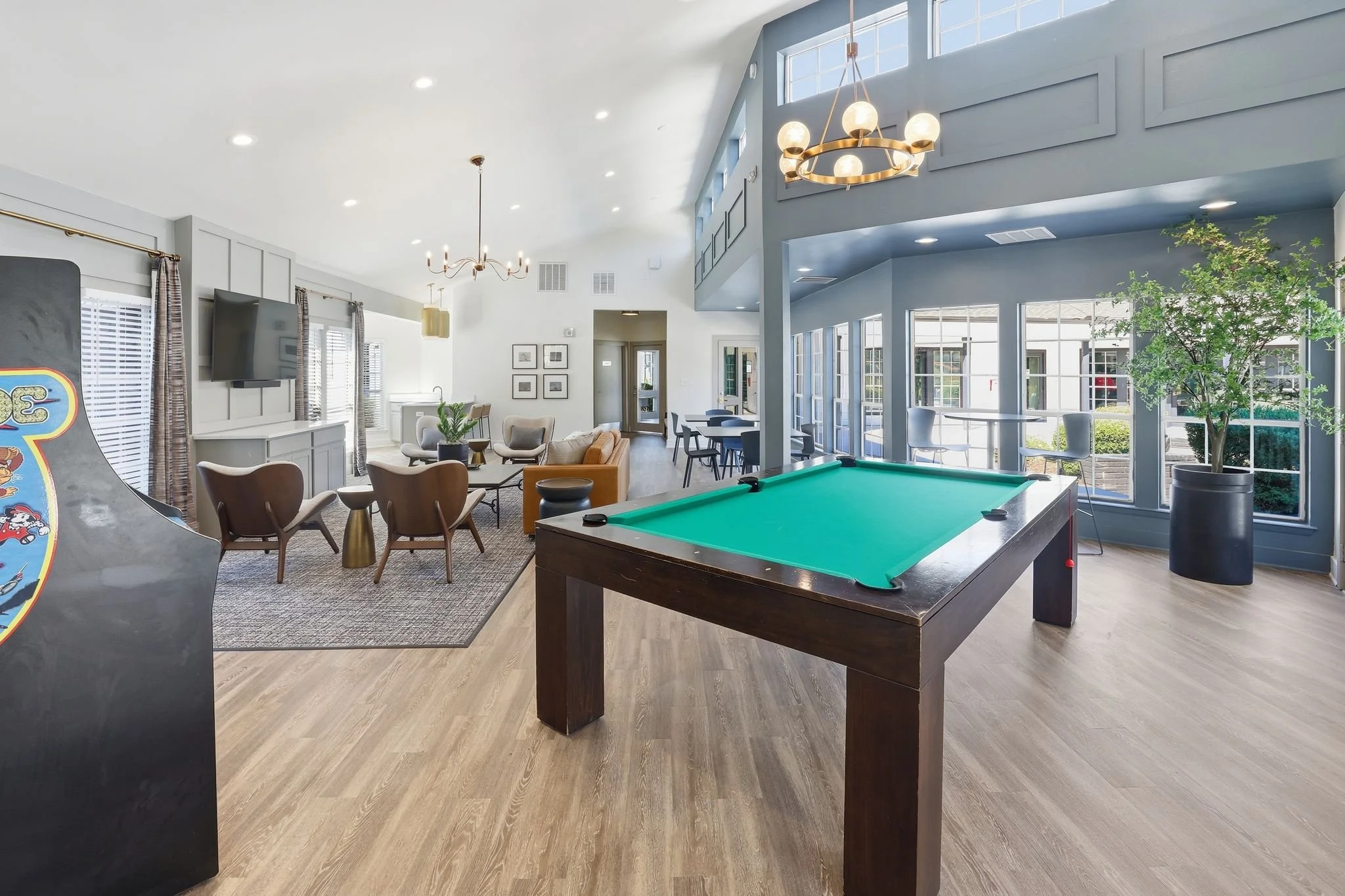 Indoor recreational room with a pool table, seating area with chairs and a sofa, large windows, and decorative lighting.