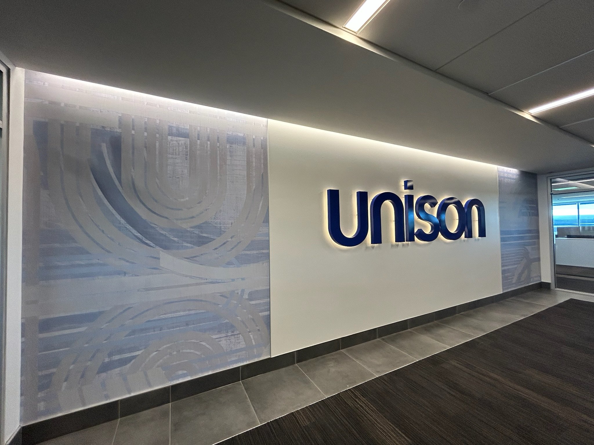 Office interior with a white wall, a large decorative glass panel, and the word 'Unisom' in large blue letters.