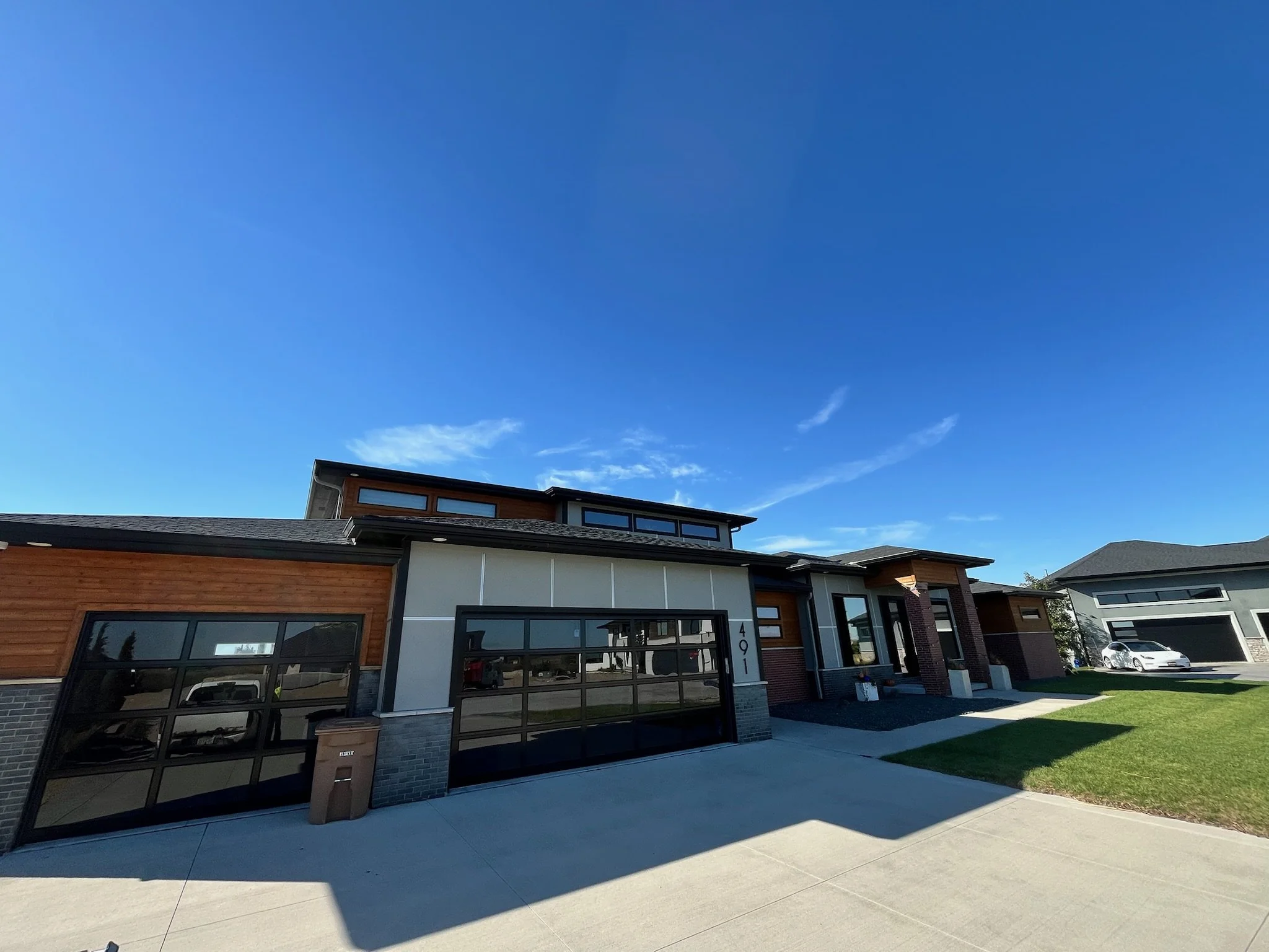 Modern residential house with a garage, large windows, and a well-maintained lawn, under a clear blue sky.