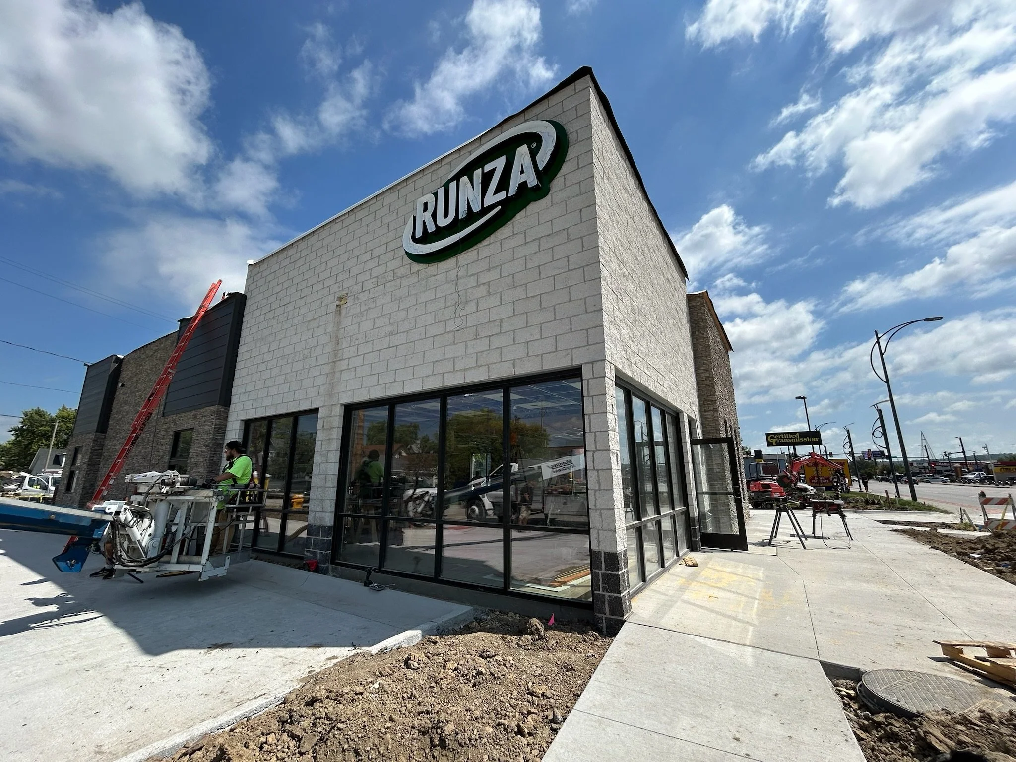 Building with a sign that reads 'RUNZ' on a cloudy sky day, part of a new commercial structure under construction with people working outside.