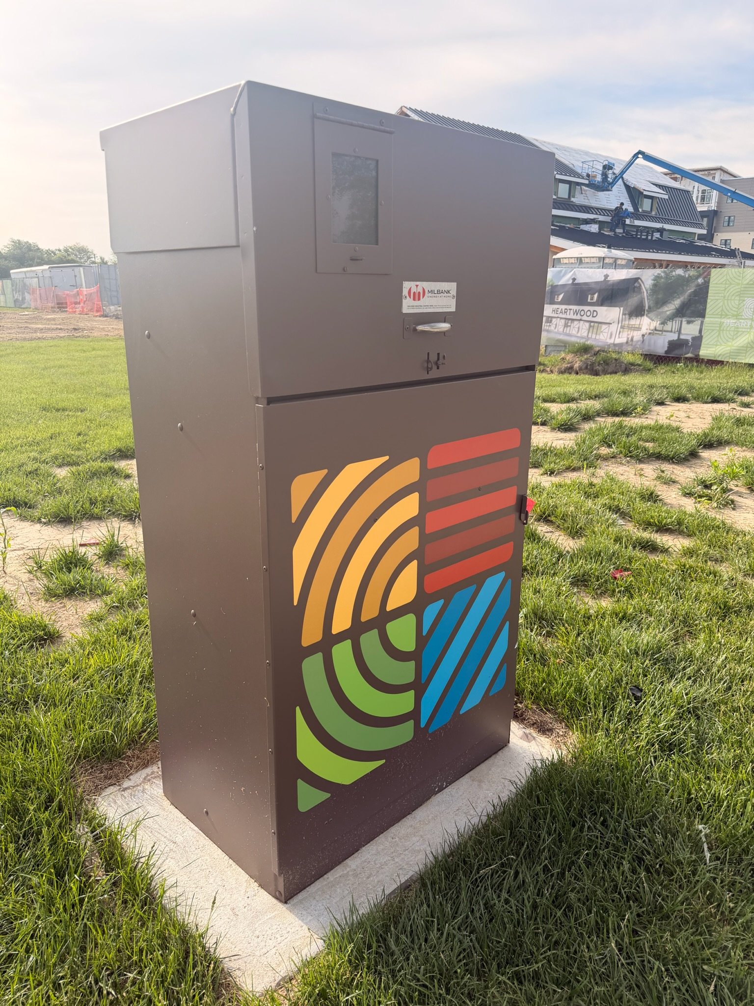 A grey utility box with a colorful fingerprint design on the front, situated on a patch of grass outdoors.