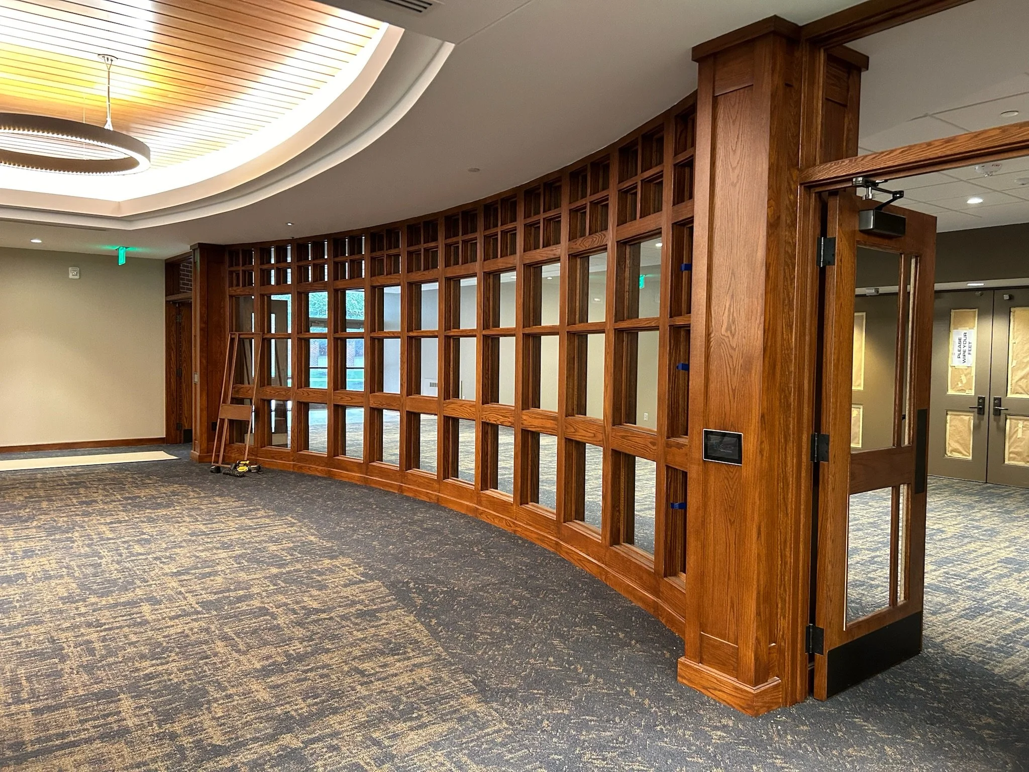 Interior view of a modern office or conference room with a wooden lattice partition, a circular ceiling light, and carpeted floor.