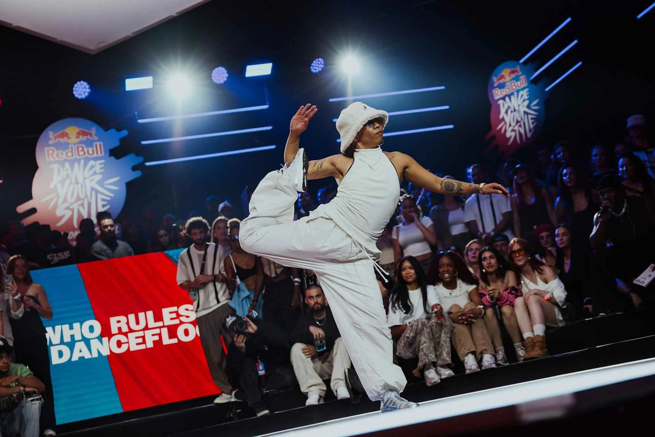 Tänzer bei Red Bull Dance Your Style Wettbewerb, umgeben von Publikum, auf einer Bühne mit Red Bull und Dance Your Style Logos im Hintergrund.