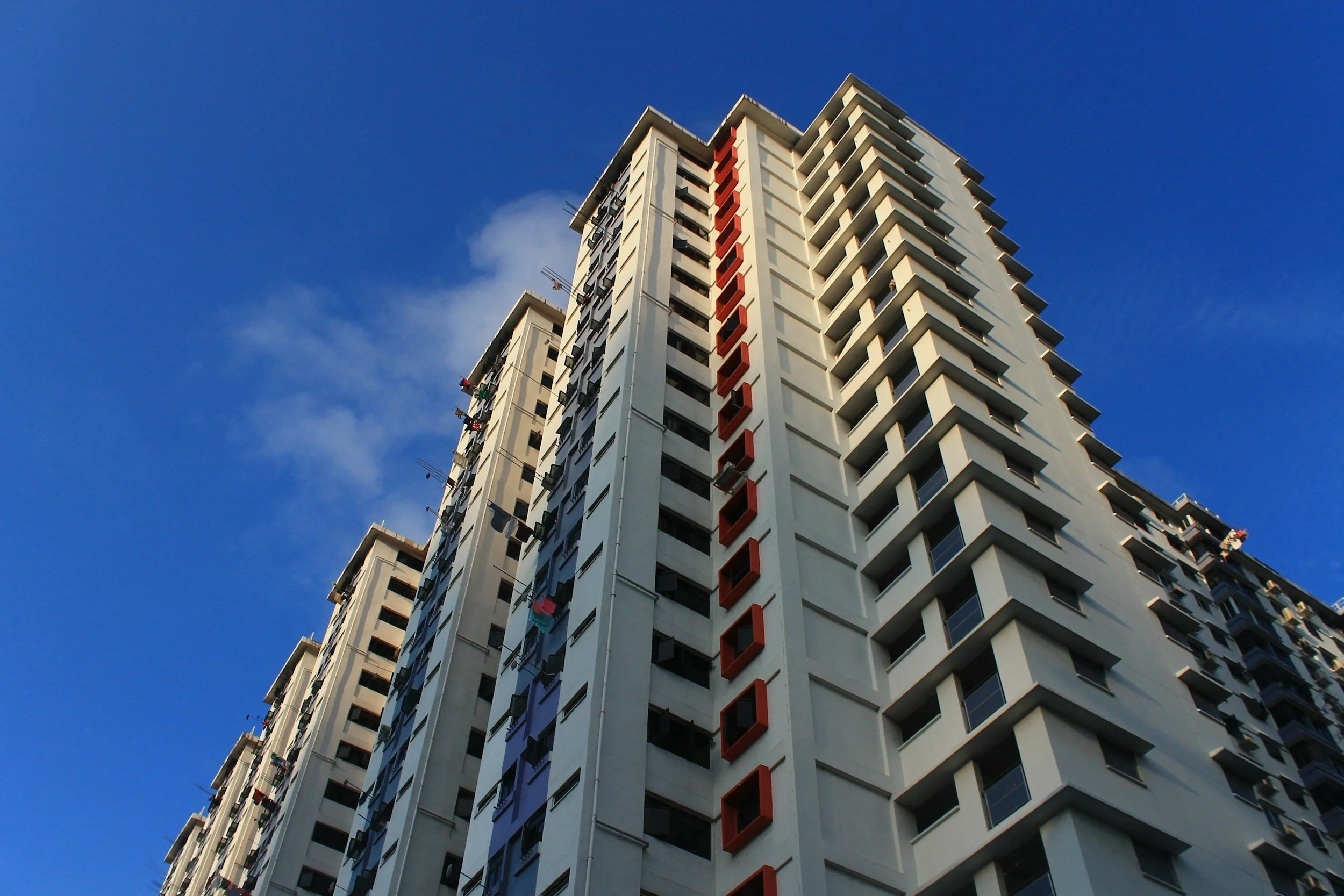 Low-angle view of a tall, modern apartment building in Charlotte, NC, with white exterior and red accents against a blue sky with a few clouds.