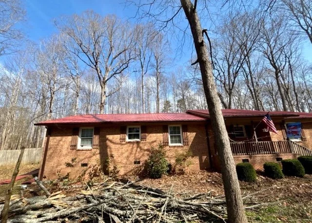 Brick house with red roof, front porch with American flag, and leafless trees in the yard and background.