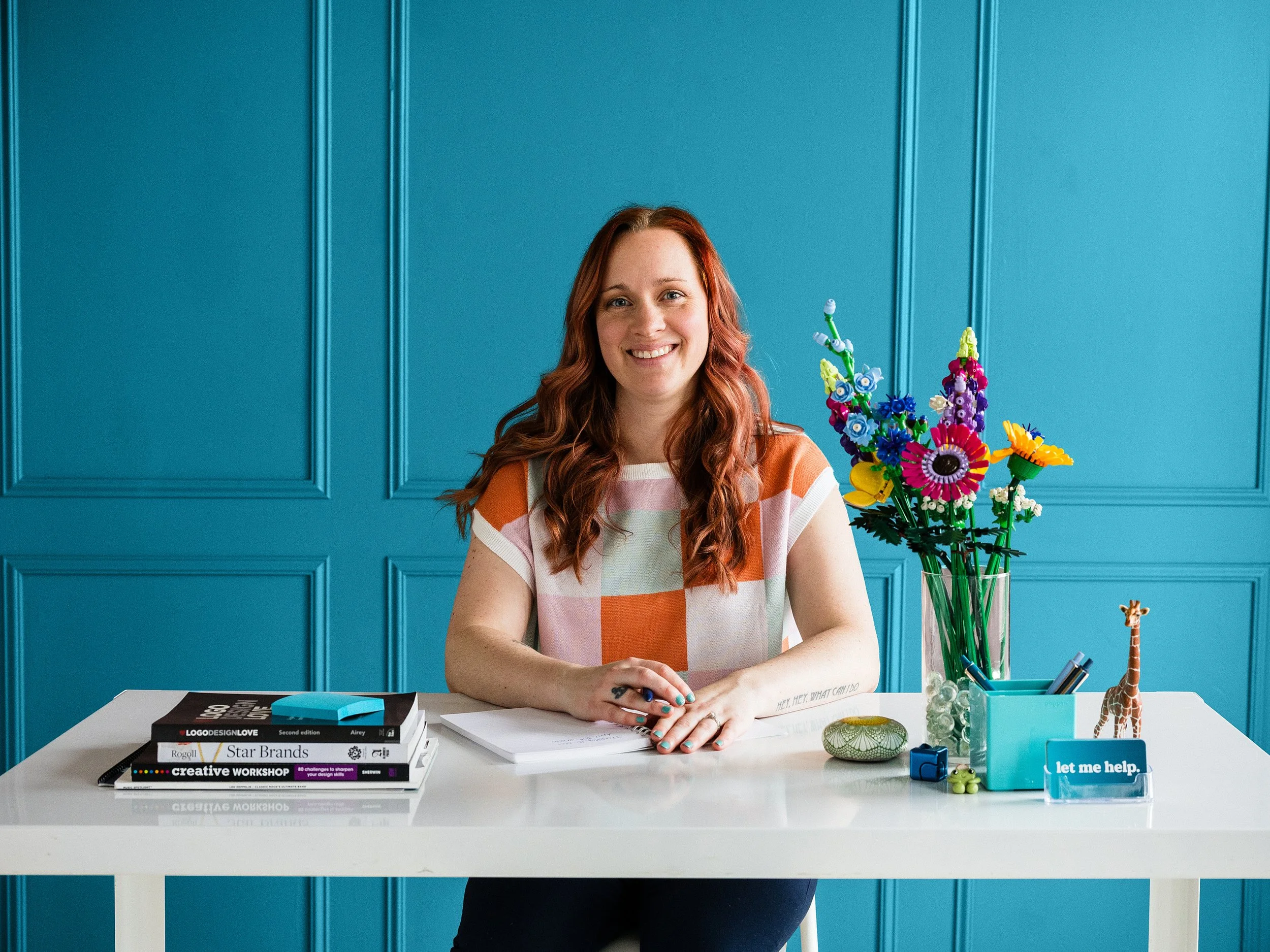 Kristen Mann sitting at a white desk smiling against a teal background