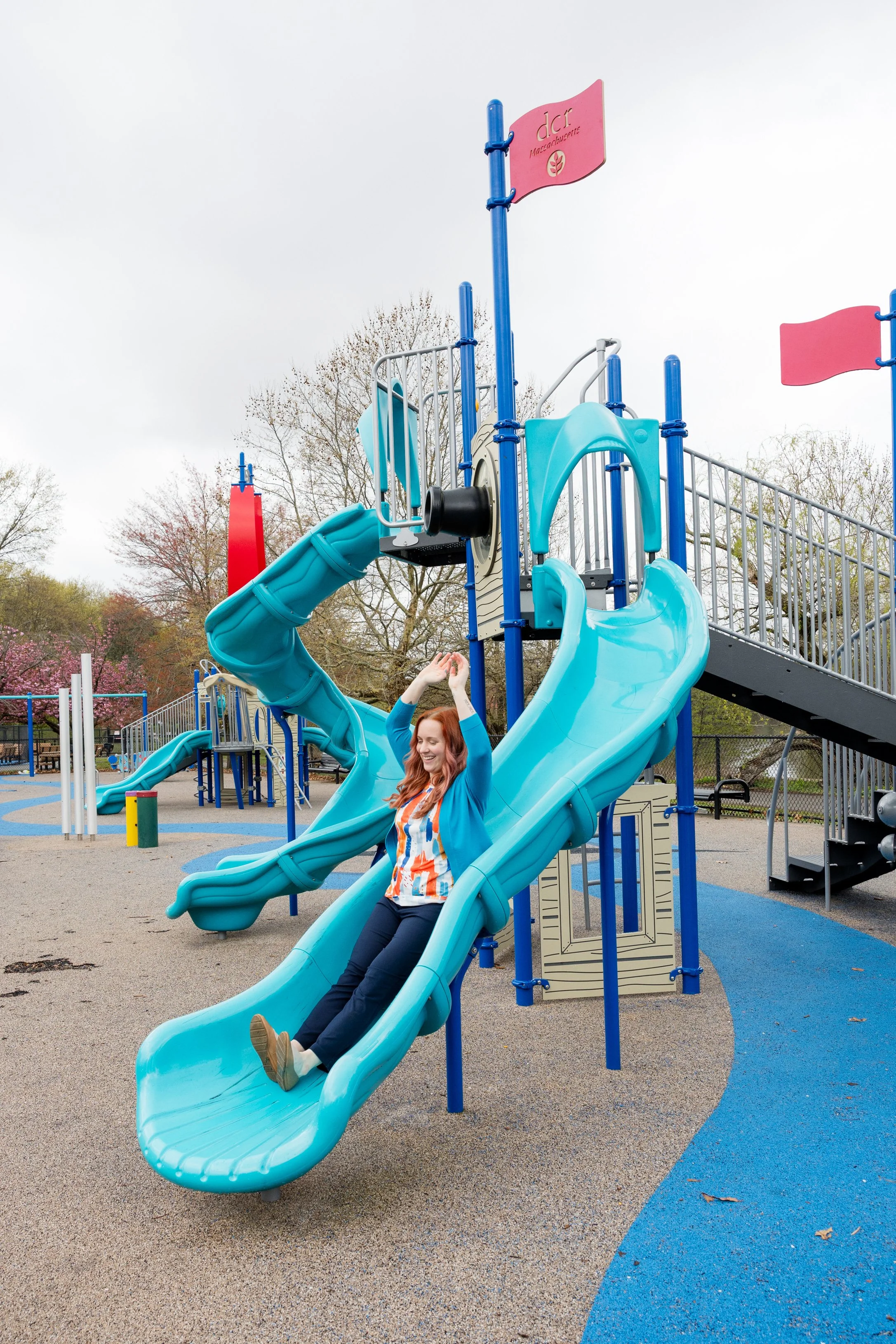 Kristen smiling while sliding down a teal blue slide