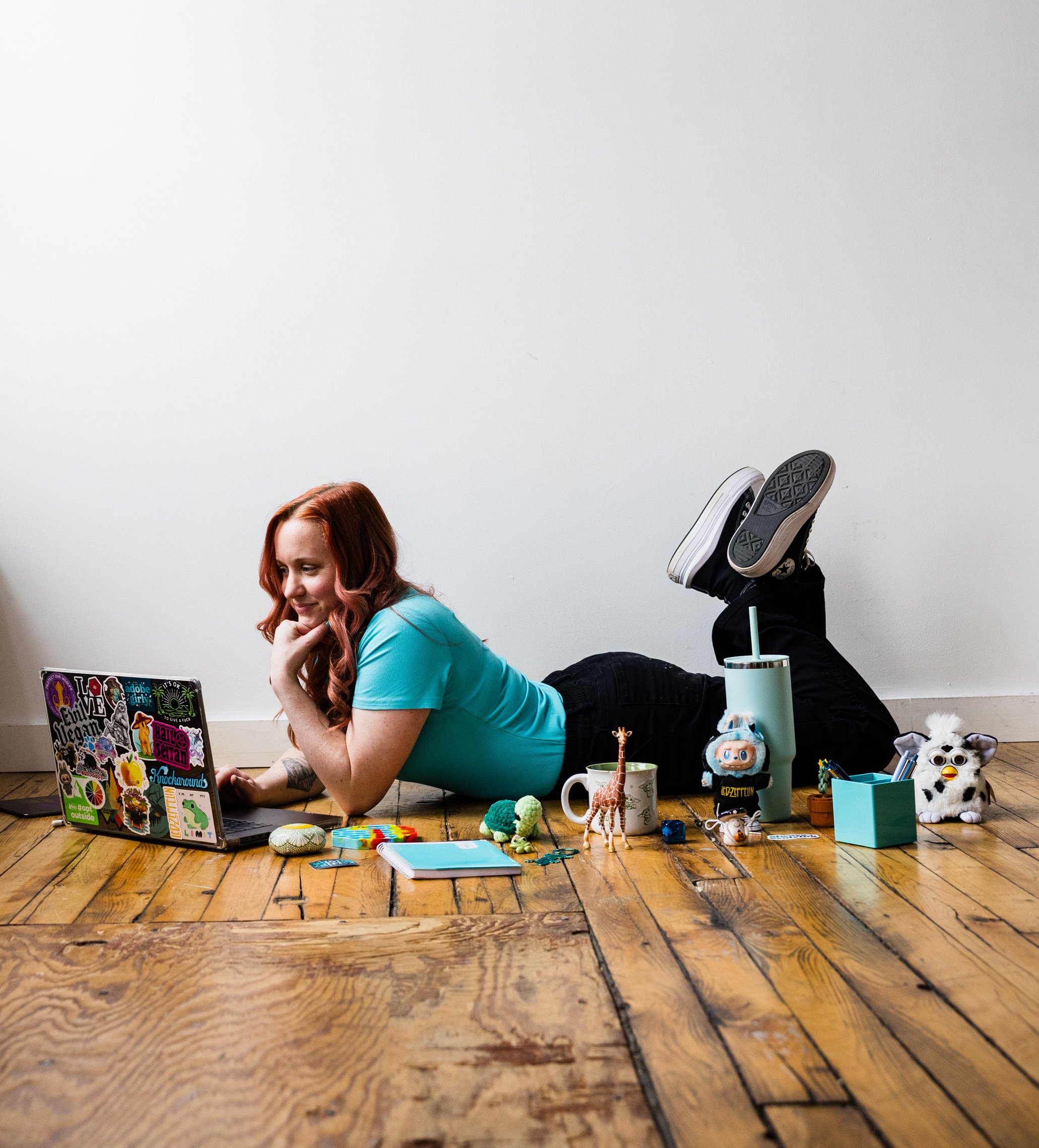 Kristen Mann laying on the wood floor working on her laptop surrounded by various trinkets