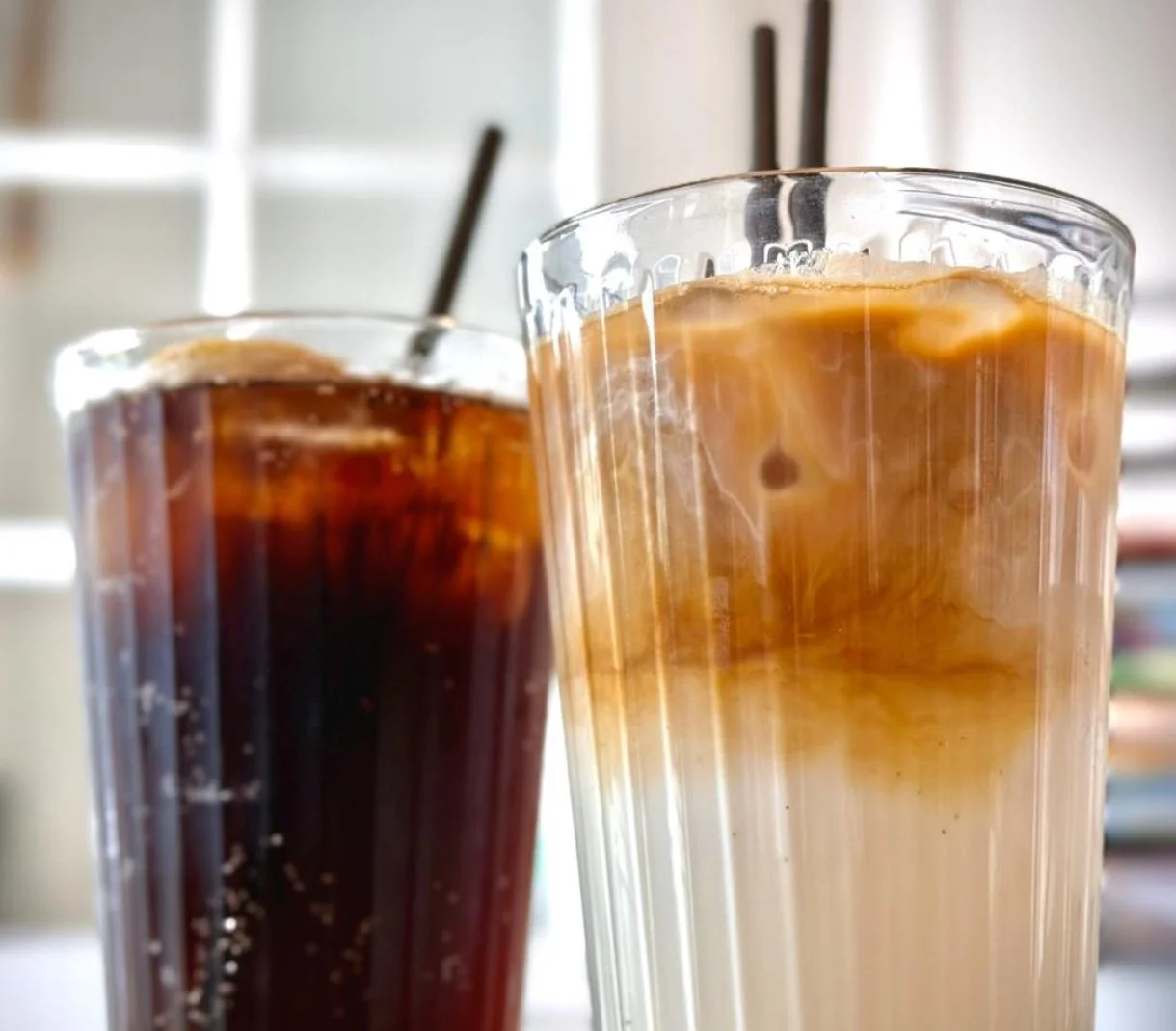 Two glasses of iced coffee, one with dark coffee and the other with caramel-colored coffee, with metal straws in each glass.