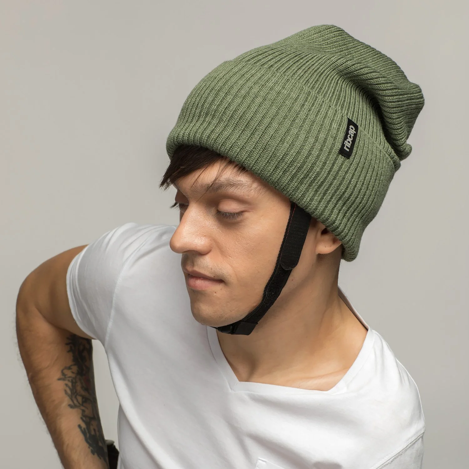 A young man wearing a green knit beanie and a white t-shirt, looking downward with closed eyes.