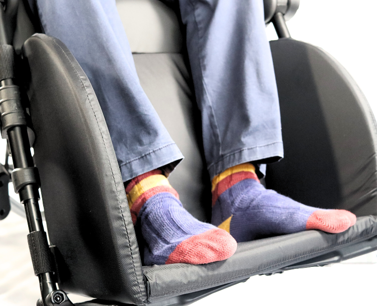Person in pants and colorful socks sitting on a black wheelchair seat.