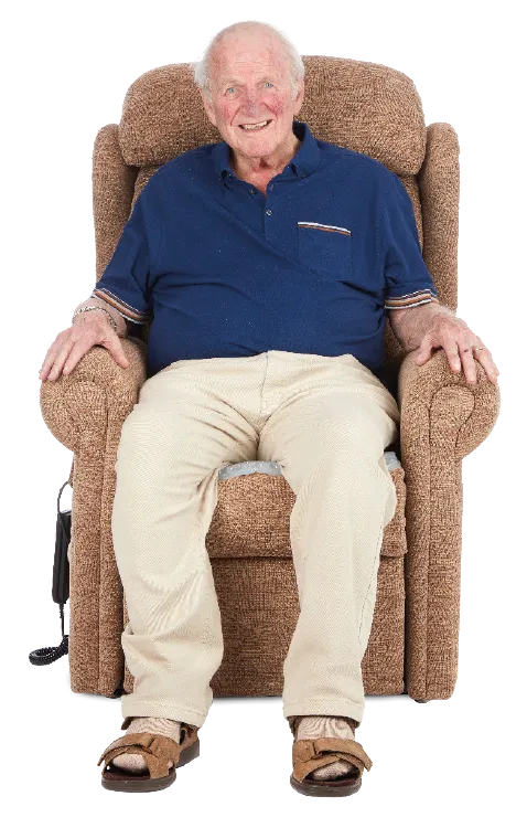 An elderly man sitting happily in a brown armchair, wearing a blue polo shirt, beige pants, and brown sandals, with a cheerful expression.