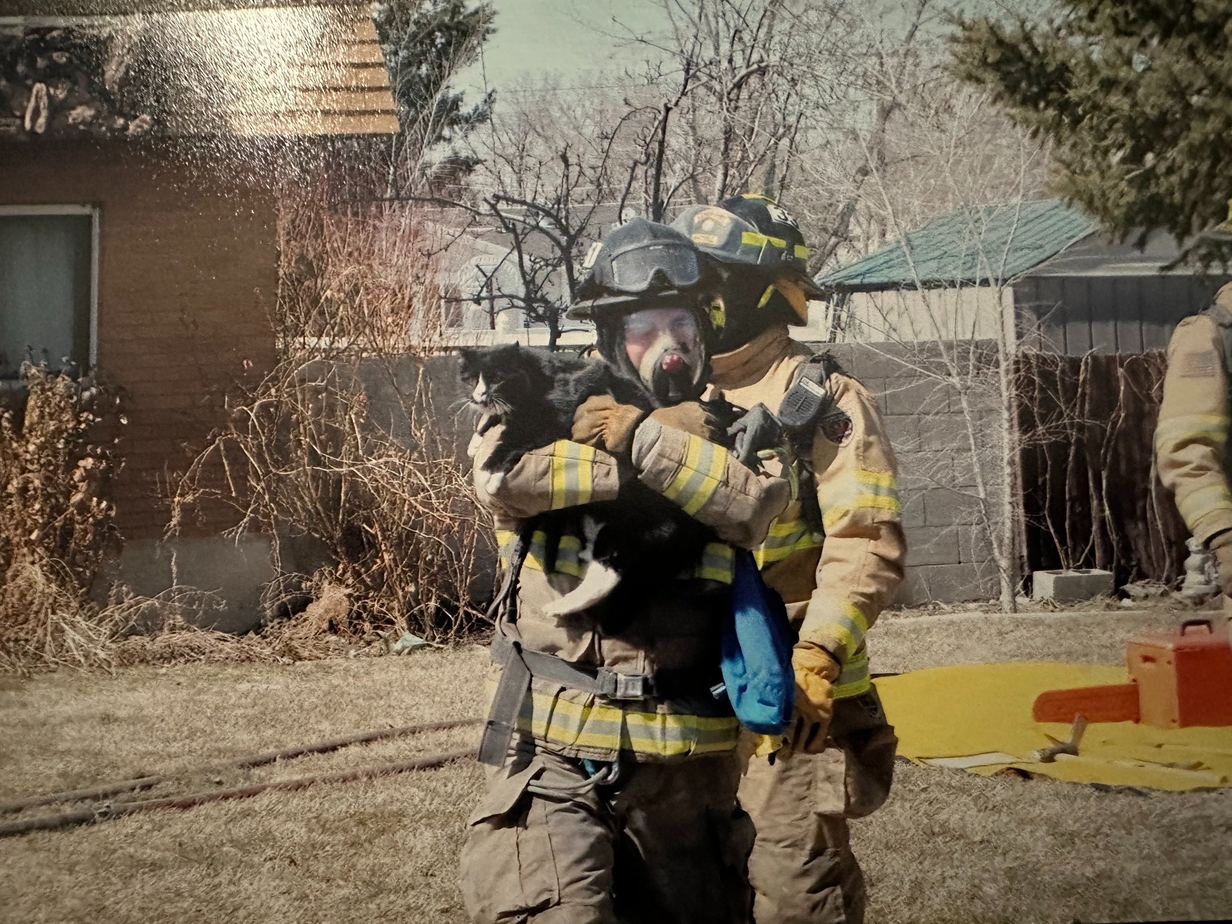 A a photo of Zach Robinson as a firefighter carrying a black and white cat away from the scene of a fire