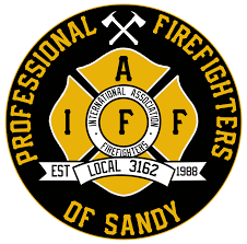 A round emblem with a black and yellow color scheme. It features two crossed axes above the letters "IAFF," and text reading "Professional Firefighters of Sandy, Local 3162, Est 1988." The center says "International Association of Firefighters.